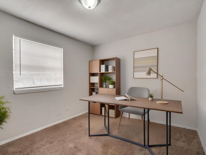 Modern home office featuring a sleek wooden desk with a stylish lamp, comfortable chair, and decorative shelving in a bright, airy room.