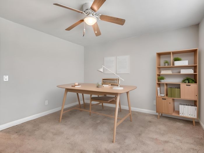 Bright and inviting home office with elegant wooden desk, modern bookshelf, and ceiling fan, perfect for productivity and style.