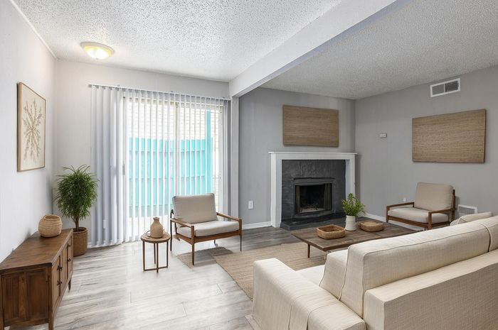 Contemporary living room with a cozy fireplace, soft beige sofa, and modern decor, filled with natural light from large windows.