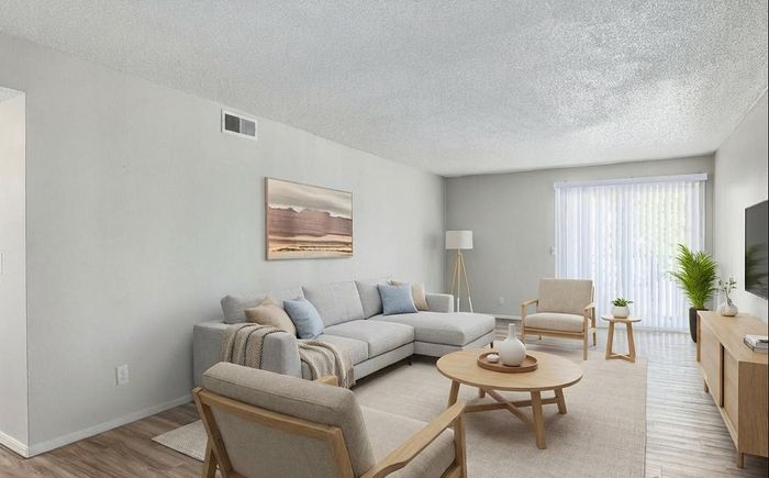 Modern living room featuring a cozy gray sectional sofa, light wood furnishings, and abundant natural light from large sliding doors with vertical blinds.