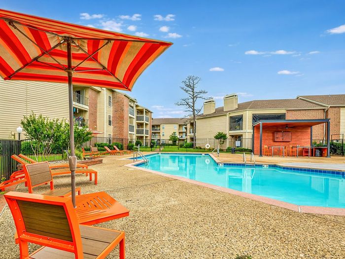 Vibrant apartment community pool with colorful lounge chairs, shaded seating, and modern amenities amidst beautiful architecture.