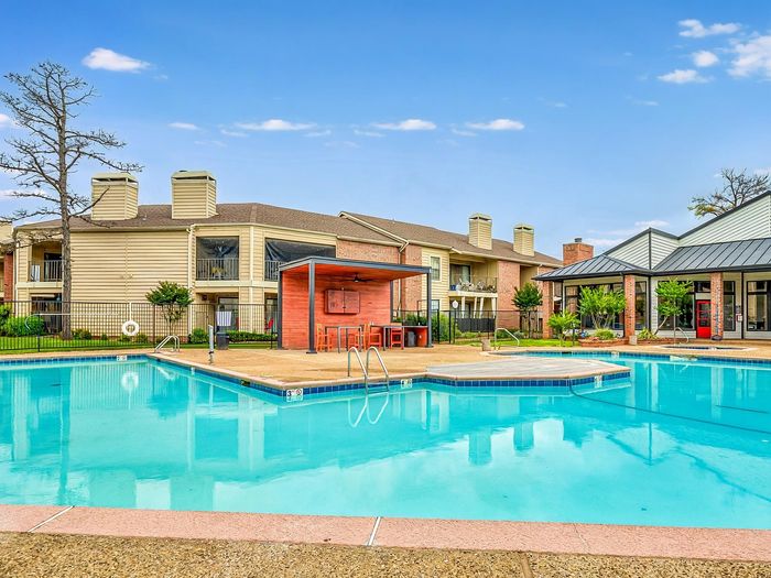 Inviting apartment complex showcasing a sparkling swimming pool, modern lounge area, and stylish building exteriors under a clear blue sky.