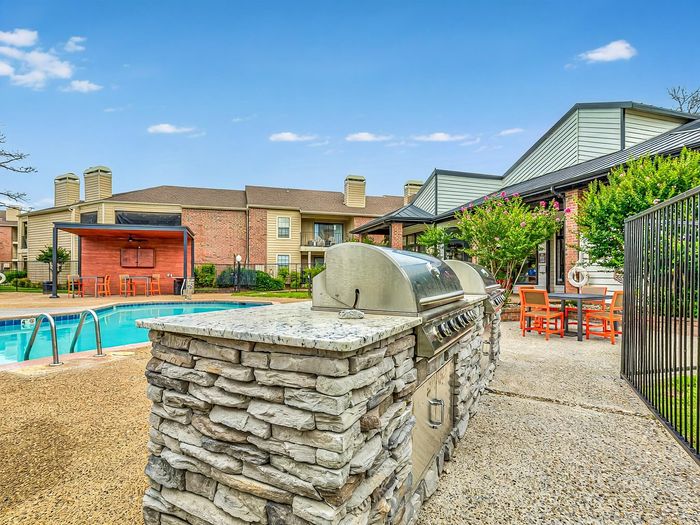 Luxurious outdoor area featuring a sparkling pool, stylish barbecue grills, and modern seating in a vibrant apartment community.