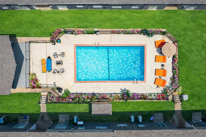 Aerial view of a luxurious outdoor pool surrounded by vibrant green lawns, colorful flowers, and stylish lounge chairs, perfect for relaxation and summer fun.