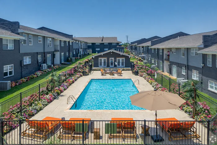 Charming apartment complex with a sparkling swimming pool surrounded by vibrant flower gardens and stylish seating areas.