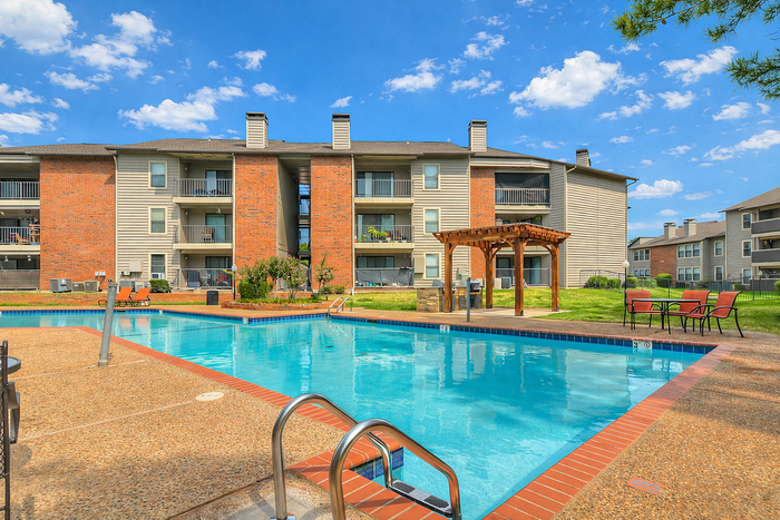 Charming apartment complex with a sparkling outdoor pool, elegant pergola, and vibrant green landscaping, perfect for relaxation and leisure.