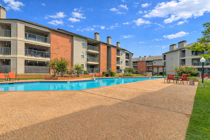 Beautiful apartment complex with inviting pool, lush greenery, and modern architecture under a clear blue sky.
