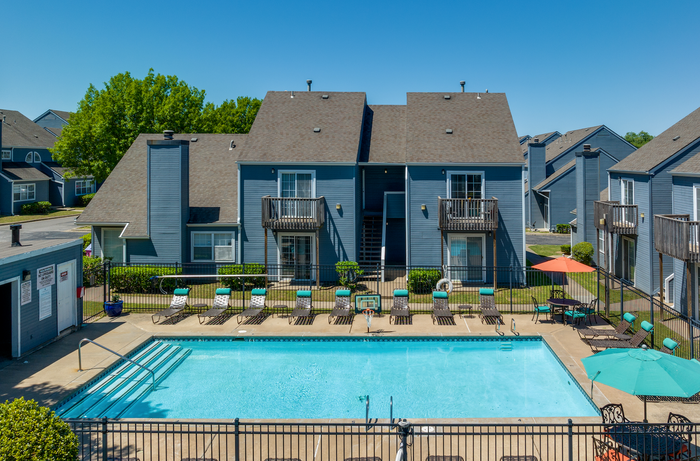 Charming apartment complex with inviting outdoor pool, surrounded by sun loungers and blue buildings under a clear sky.