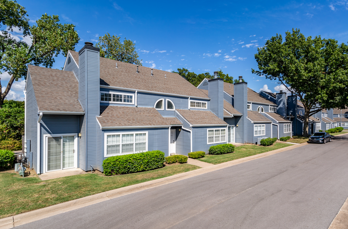 Charming townhouse community with modern architecture, featuring unique rooflines and welcoming facades, surrounded by lush greenery under a clear blue sky.
