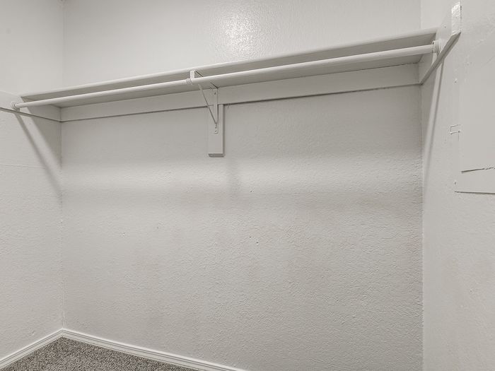 Spacious walk-in closet with a sleek built-in hanging rod and textured walls, perfect for ample storage and organization.