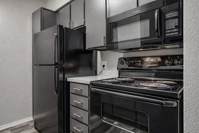 Modern kitchen with sleek black appliances, featuring a refrigerator, oven, and microwave, complemented by stylish dark cabinetry and elegant countertops.