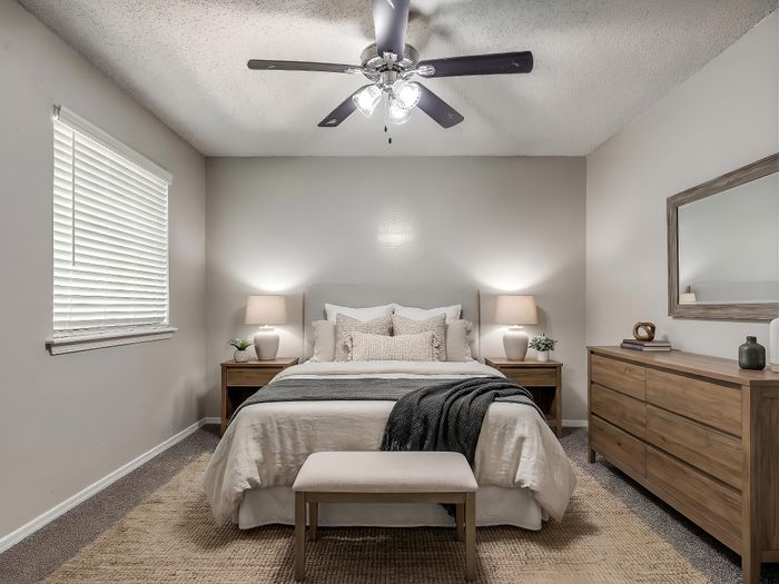 Elegant bedroom featuring a cozy bed with plush pillows, wooden nightstands, and a stylish dresser, all enhanced by soft lighting and a chic ceiling fan.
