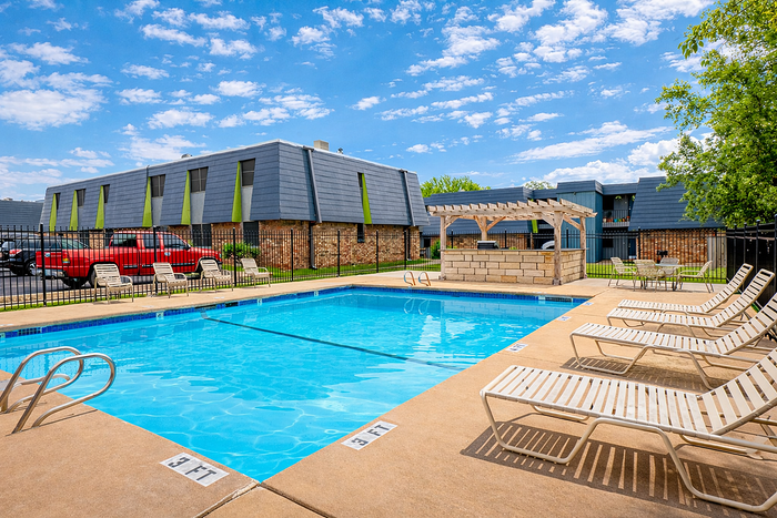 Inviting apartment outdoor area featuring a refreshing swimming pool, elegant lounge chairs, and charming pergola seating under a vibrant blue sky.