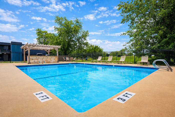 Inviting outdoor pool area with sparkling blue water, surrounded by lush greenery and relaxing lounge chairs under a vibrant sky.