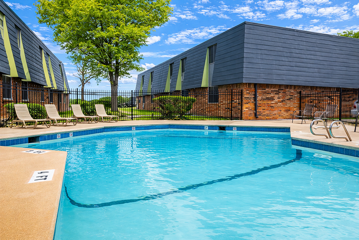 Inviting outdoor swimming pool with sun loungers and modern apartment buildings under a bright blue sky.