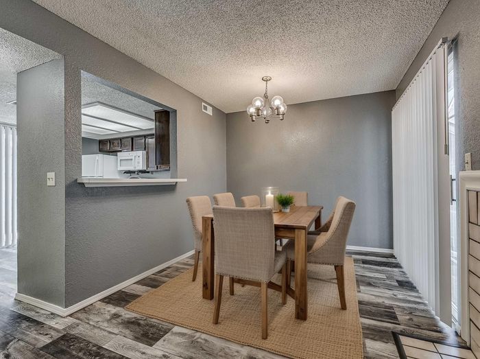 Chic dining area with elegant lighting, featuring a wooden table and cushioned chairs, adjacent to a modern kitchen pass-through.