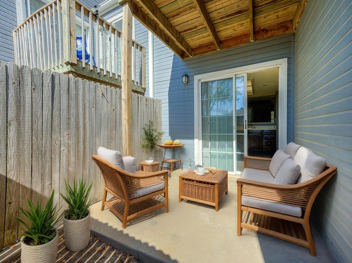 Charming outdoor patio with cozy wicker furniture, ideal for relaxation, complemented by green plants and a sliding glass door leading inside.