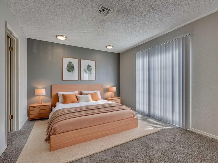 Elegant bedroom with modern decor, featuring a cozy bed with orange accents, soft lighting, and large vertical blinds for natural light.