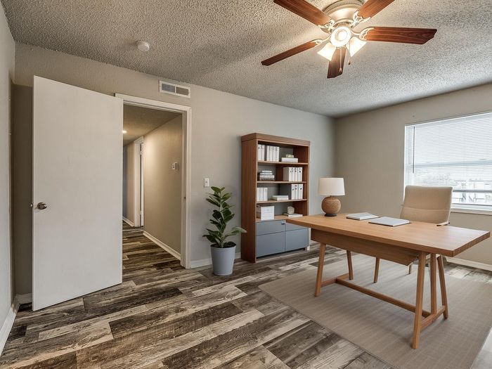 Modern home office with sleek wooden desk, organized shelves, and elegant ceiling fan, offering a bright and productive work environment.