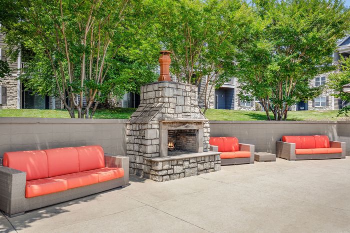 Charming outdoor space with stylish stone fireplace, vibrant orange seating, and lush greenery, perfect for relaxation and social gatherings.