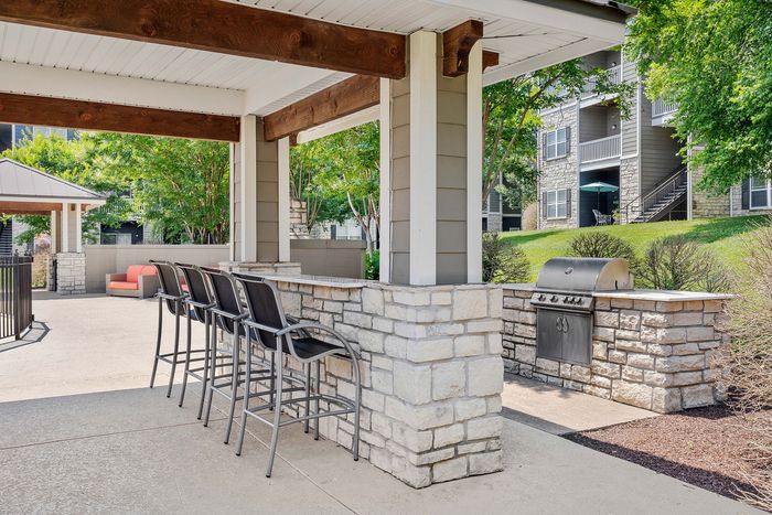 Charming outdoor kitchen and seating area featuring a sleek barbecue grill, spacious bar with stools, and lush green surroundings.