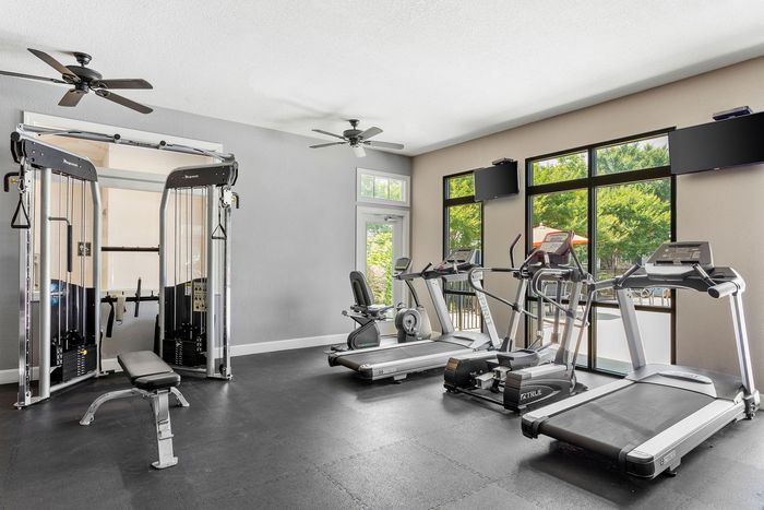 Bright and modern fitness center with state-of-the-art exercise equipment, including treadmills, stationary bike, and weight machine, overlooking a lush outdoor view through large windows.