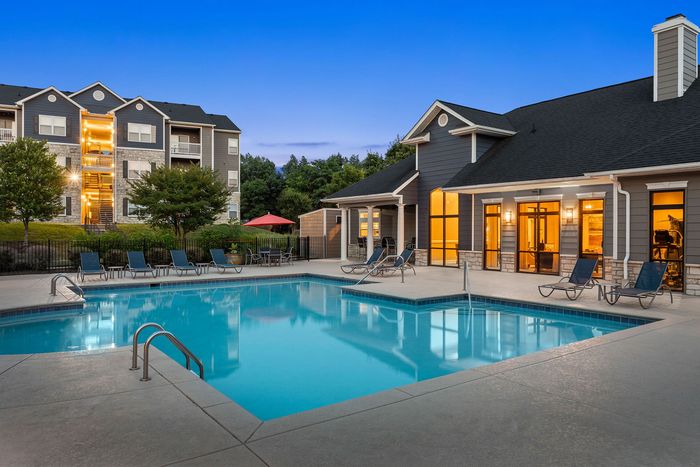 Inviting apartment complex featuring a sparkling outdoor swimming pool, modern lounge chairs, and charming architecture set against lush greenery.