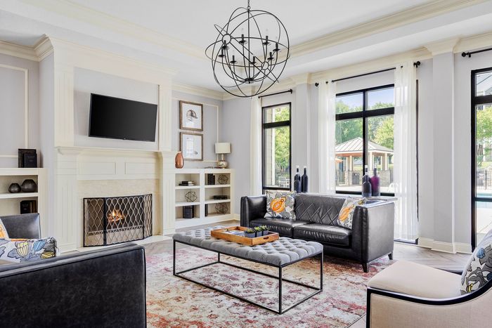 Elegant living room with modern chandelier, plush leather sofas, and a cozy fireplace, featuring large windows offering a bright poolside view.