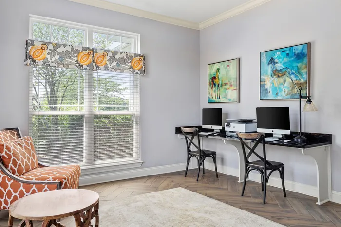 Bright home office featuring a double workstation with modern decor, vibrant artwork, and a cozy reading nook.