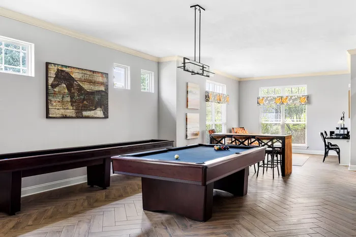 Bright recreational room featuring a pool table, shuffleboard, and stylish decor with modern artwork and large windows.
