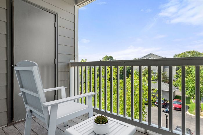 Charming balcony view featuring modern outdoor seating, lush greenery, and a serene residential backdrop under a clear blue sky.