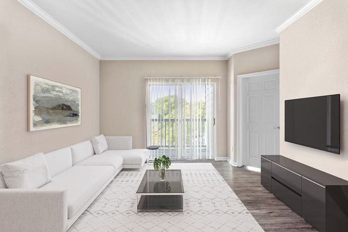 Bright and modern living room featuring a sleek white sofa, large wall-mounted TV, and floor-to-ceiling windows with soft natural light.