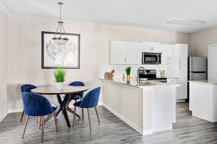 Bright and modern kitchen dining area featuring elegant white cabinets, a sleek marble countertop, stylish blue velvet chairs, and contemporary decor.
