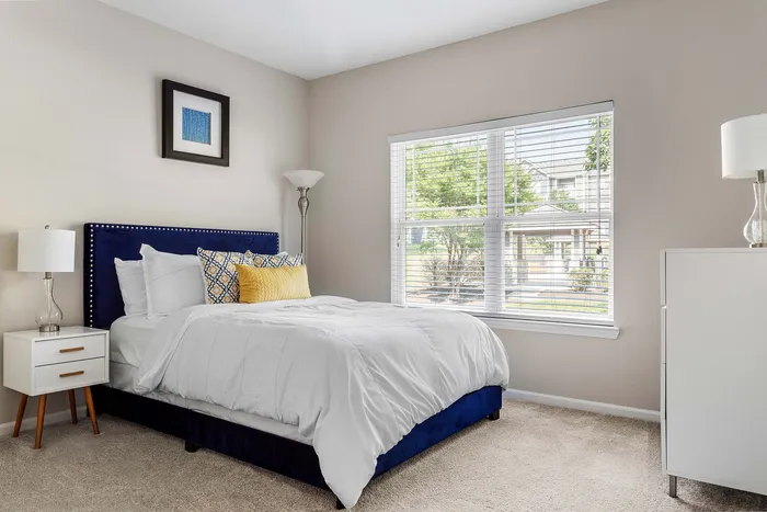 Bright and inviting bedroom with a plush navy bed, elegant decor, and large window with scenic view.