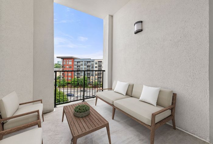 Chic apartment balcony with modern seating, offering a picturesque view of urban architecture and lush greenery.