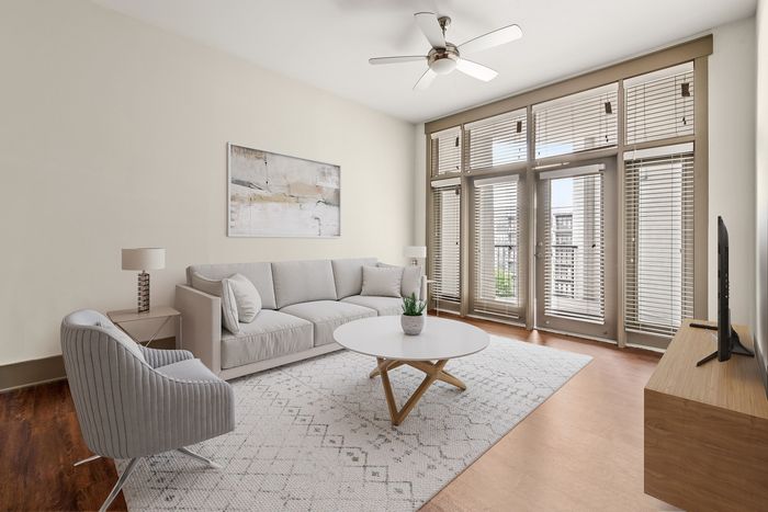 Bright and inviting living room with modern decor, cozy sofa, large windows with blinds, and a stylish ceiling fan.