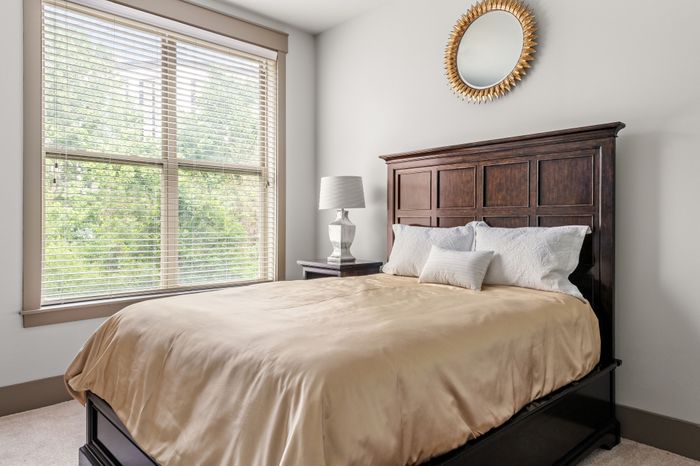 Bright and cozy bedroom with a large window, elegant wooden bed frame, and a stylish mirror enhancing the serene atmosphere.