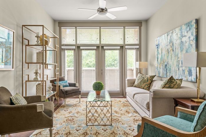 Chic living room with modern decor, featuring a comfortable sofa, stylish armchairs, and a glass coffee table, all illuminated by natural light from large windows with blinds.