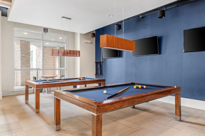 Luxurious recreation room featuring two elegant pool tables, modern decor, and ample natural light, perfect for social gatherings.