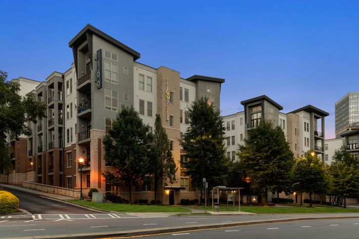 Modern urban apartment complex at dusk with lush landscaping and sleek architectural design.