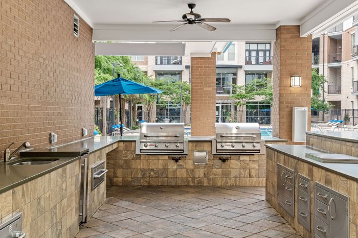 Stylish outdoor kitchen with modern stainless steel grills and elegant stone countertops, perfect for poolside entertaining in a luxury apartment complex.