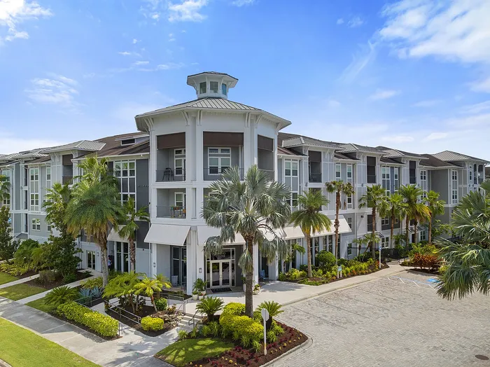 Modern luxury apartment building with elegant architecture surrounded by lush palm trees under a bright blue sky.