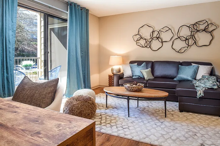 Inviting living room with stylish decor, featuring a cozy sofa, elegant wooden table, and abundant natural light from large windows draped in ocean-blue curtains.