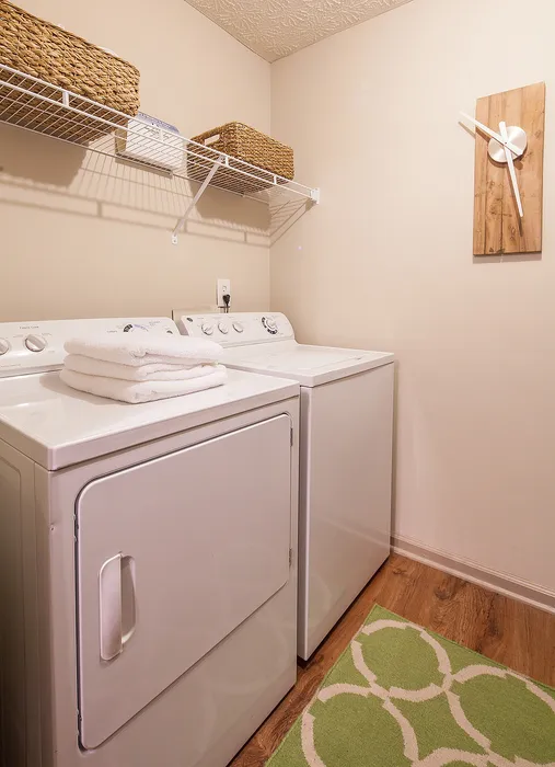 Chic and functional laundry room with modern washer and dryer, cozy green rug, and stylish wall clock.