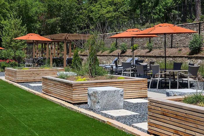 Serene outdoor space with modern seating area, lush greenery, and vibrant orange umbrellas for relaxation and social gatherings.