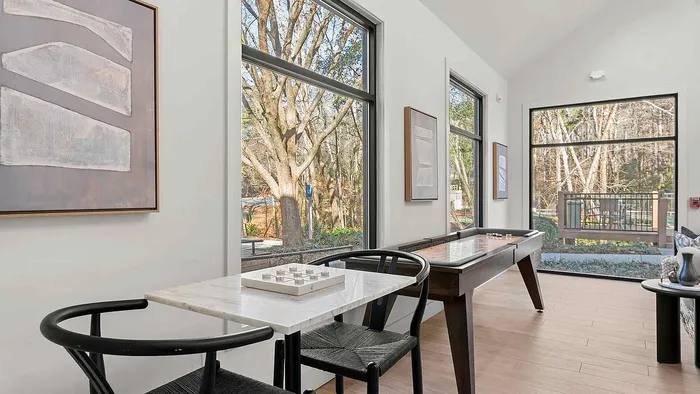 Chic recreational room with elegant board game table, large windows offering scenic forest views, and modern art adorning the walls.