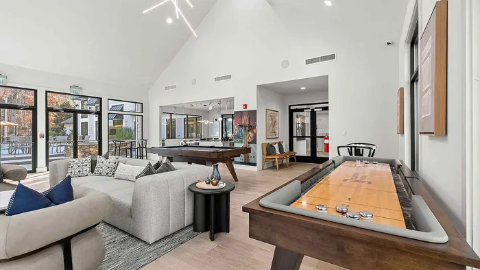Bright and modern recreational room featuring cozy seating, pool and shuffleboard tables, with large windows overlooking a stylish patio area.