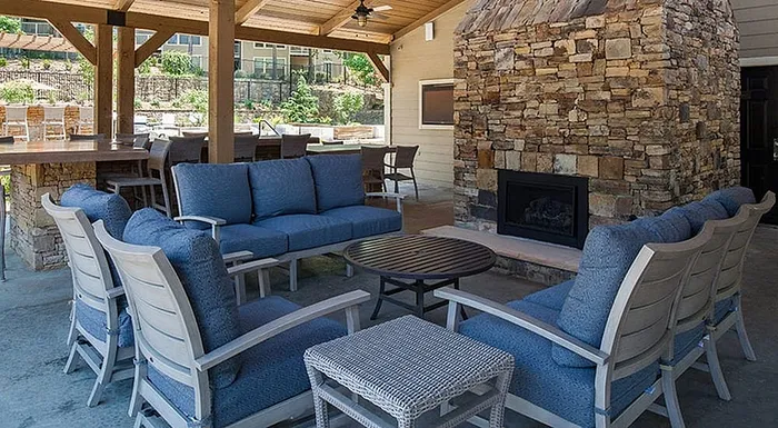 Inviting outdoor lounge area with comfortable blue cushioned seating, a cozy stone fireplace, and a stylish wooden bar setup under a charming wooden pergola.