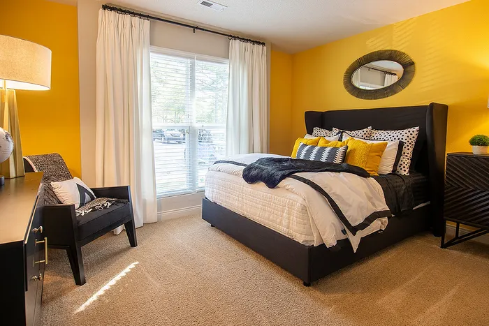 Chic bedroom with vibrant yellow accents, plush bedding, and a cozy armchair bathed in natural light.
