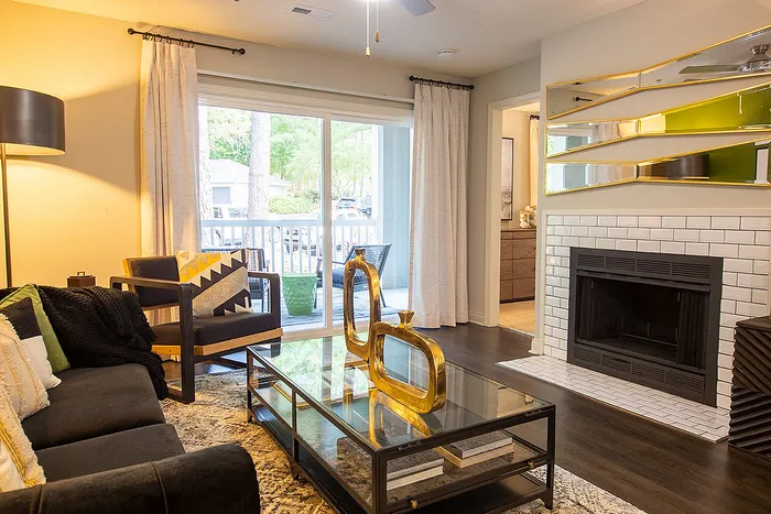 Inviting living room with elegant decor, featuring a cozy fireplace, sleek glass table, and bright natural light from large windows overlooking a tranquil balcony.